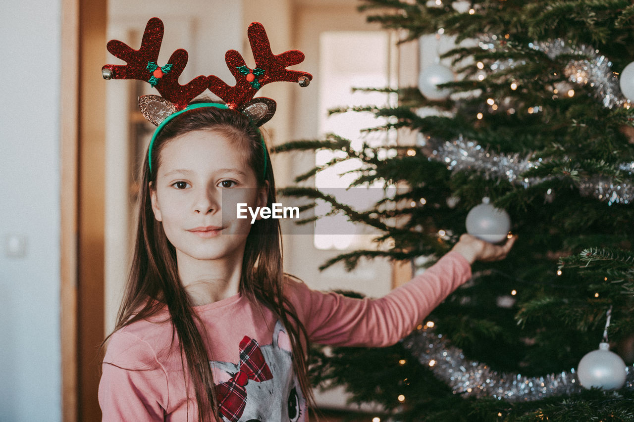 Portrait of a girl next to the new year tree, holding a christmas tree decoration in her hands 