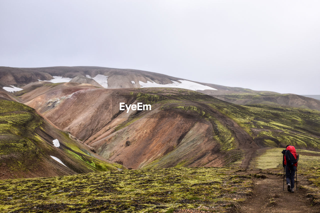 MAN WALKING ON LANDSCAPE AGAINST SKY