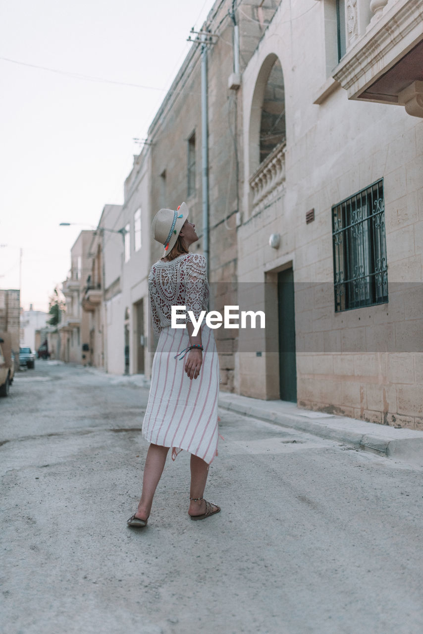 FULL LENGTH OF WOMAN STANDING ON STREET AGAINST BUILDINGS