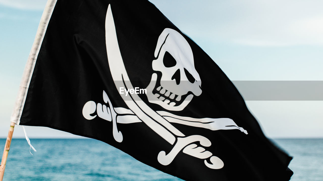 Black pirate flag with skull symbol on the desert island