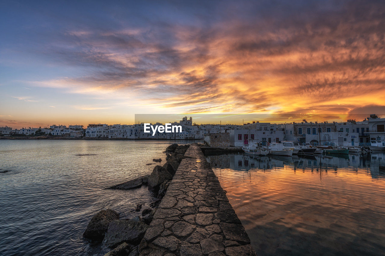 sky, water, sunset, reflection, horizon, architecture, dawn, evening, cloud, sea, city, nature, built structure, travel destinations, beauty in nature, scenics - nature, shore, building exterior, landscape, coast, pier, afterglow, sunlight, travel, outdoors, building, urban skyline, no people, dramatic sky, cityscape, tranquility, nautical vessel, environment, twilight, transportation, tourism, land, harbor, dock, beach, ocean, sun, body of water