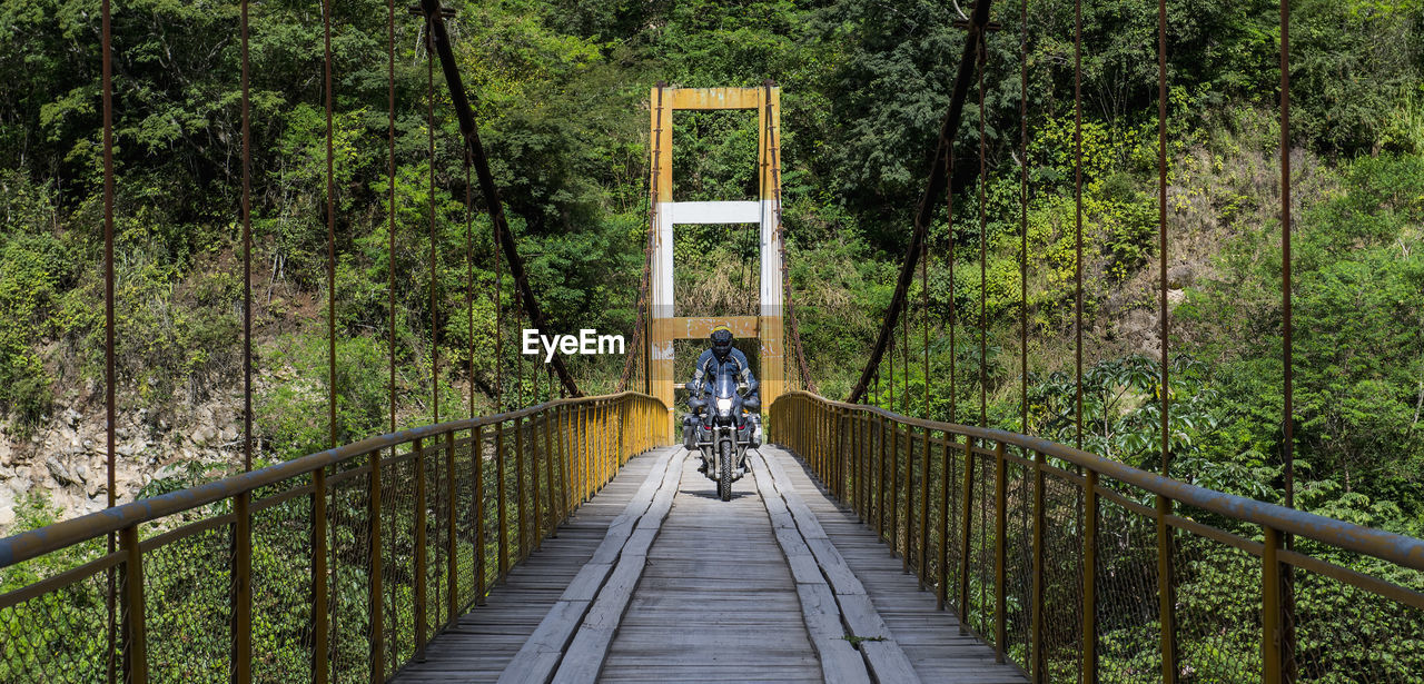 Man driving touring motorbike on suspension bridge in peru