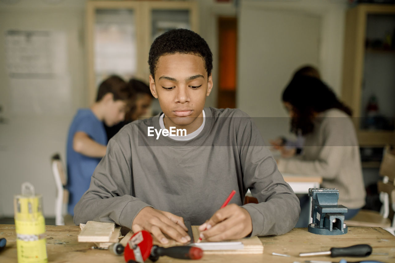 Focused male teenage student measuring wood during carpentry class at high school