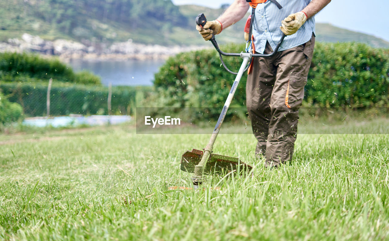 Crop elderly man mowing grass in backyard with lawn mower in lakeside