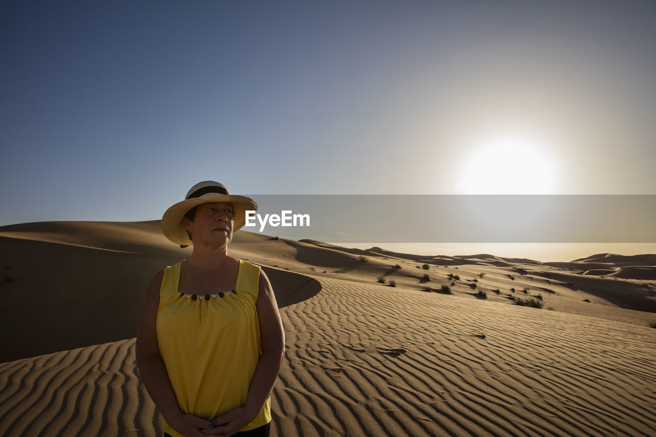 WOMAN STANDING ON SAND DUNE AGAINST SKY