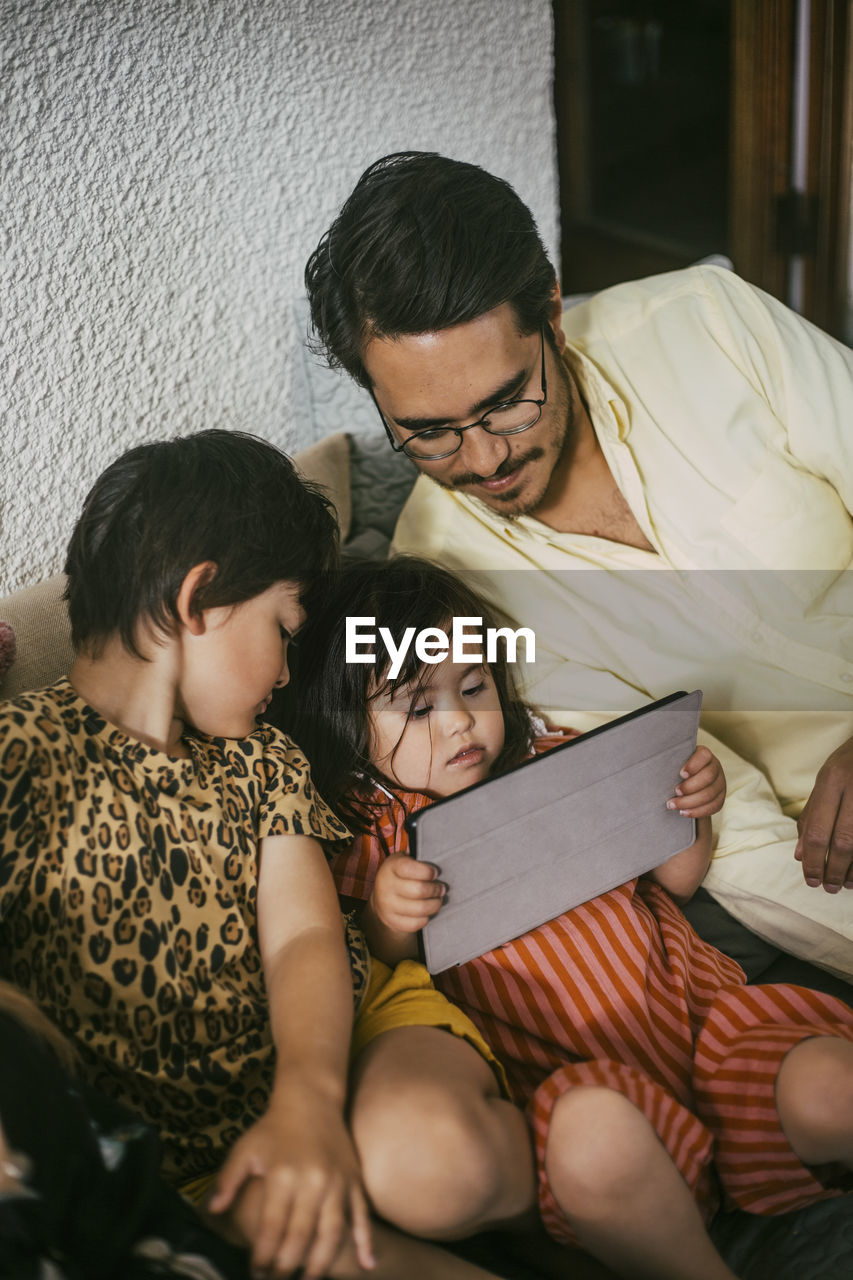 Down syndrome daughter using digital tablet by father and sister on sofa at home