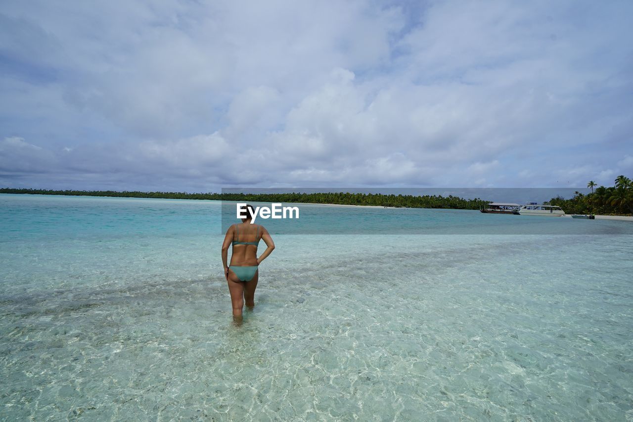 REAR VIEW OF SHIRTLESS MAN STANDING AT BEACH