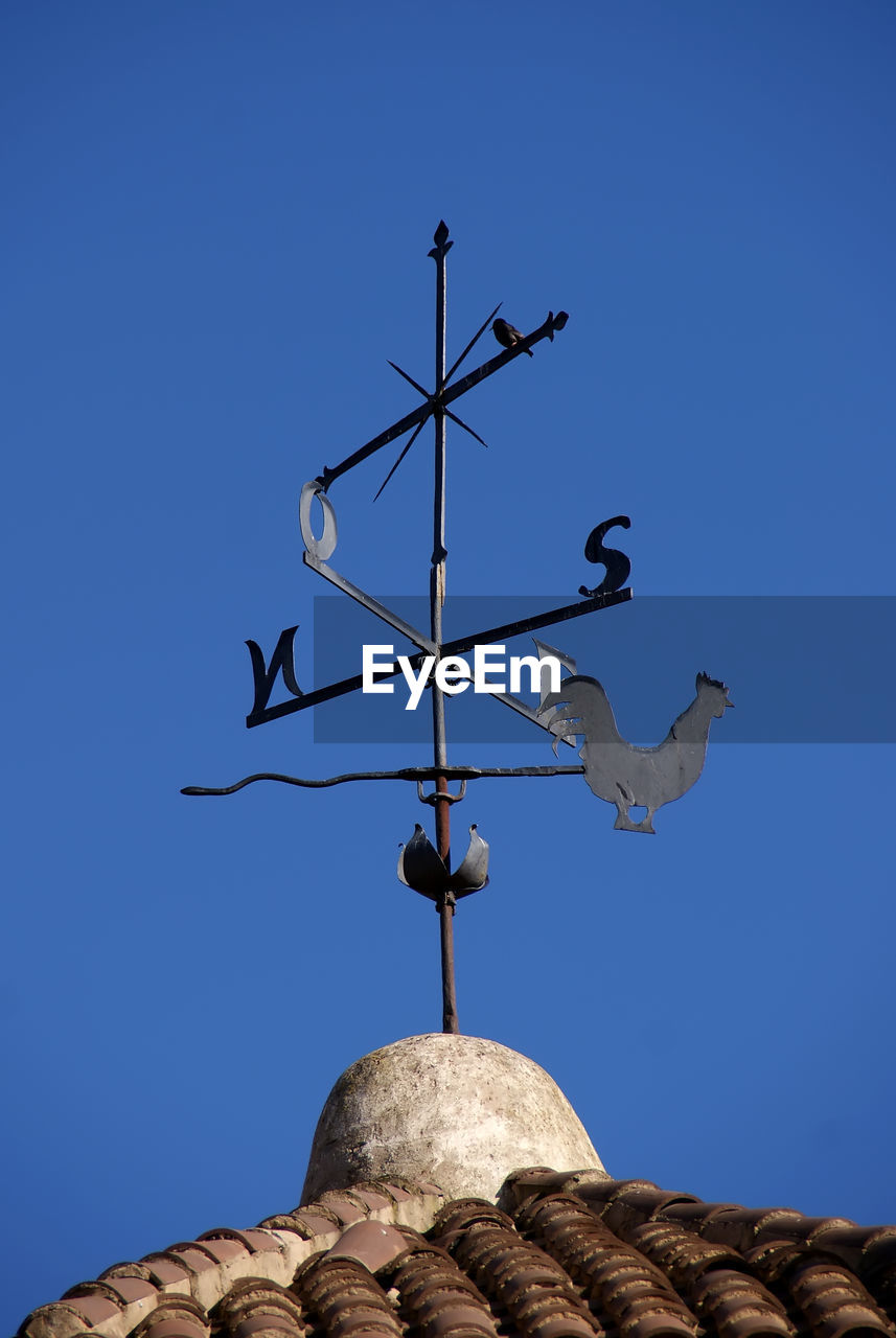 Low angle view of weather vane on roof against clear blue sky