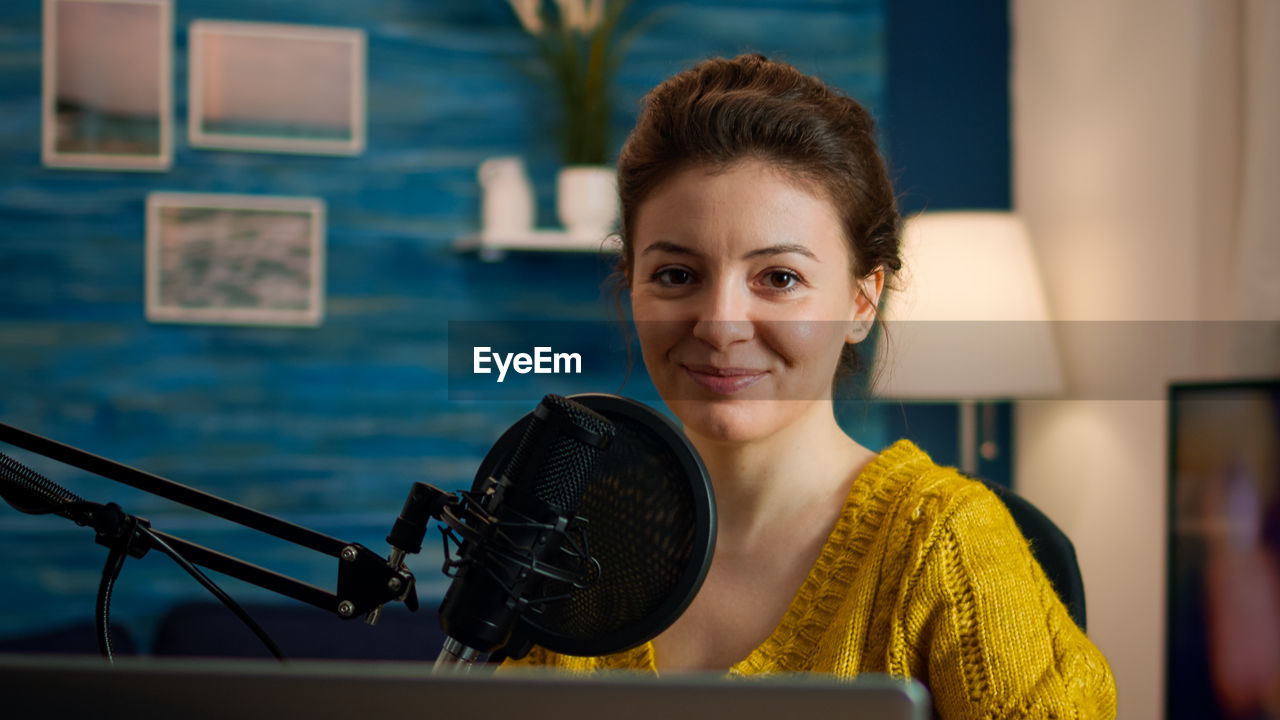 Portrait of a smiling young woman podcasting at home