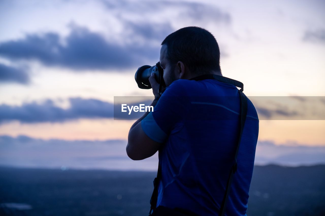 Rear view of photographer photographing against sky during sunset