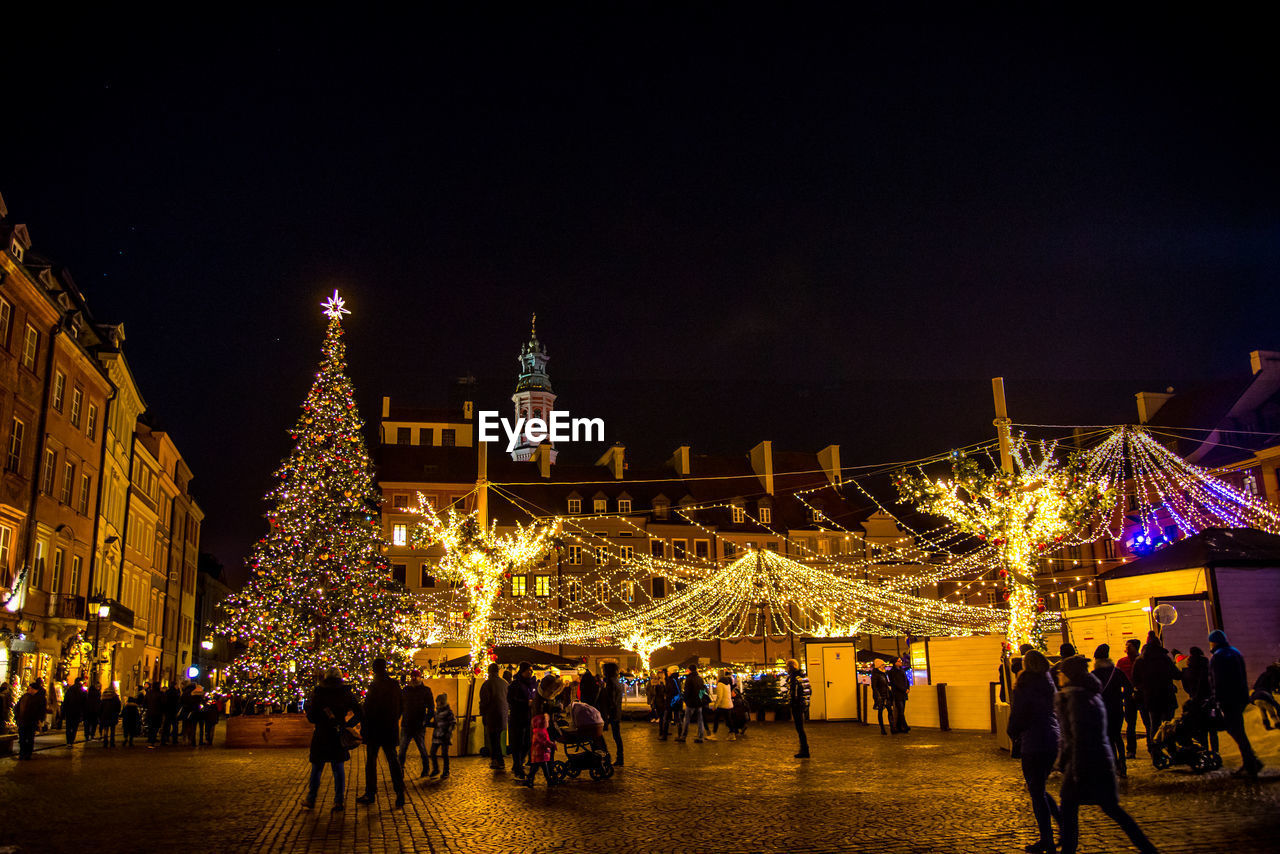 GROUP OF PEOPLE AT ILLUMINATED CHRISTMAS LIGHTS AT NIGHT