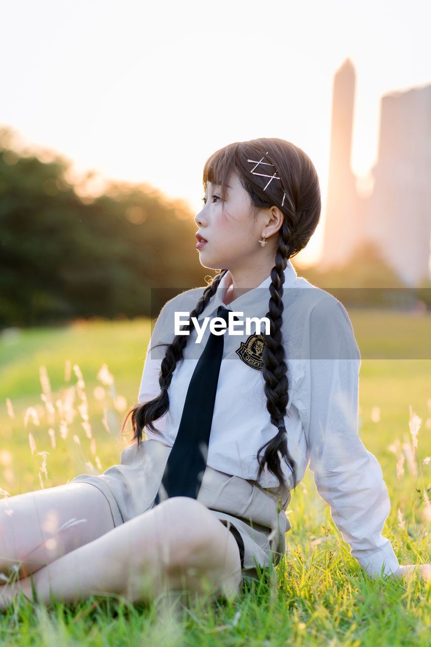 WOMAN LOOKING AWAY WHILE SITTING ON LAND