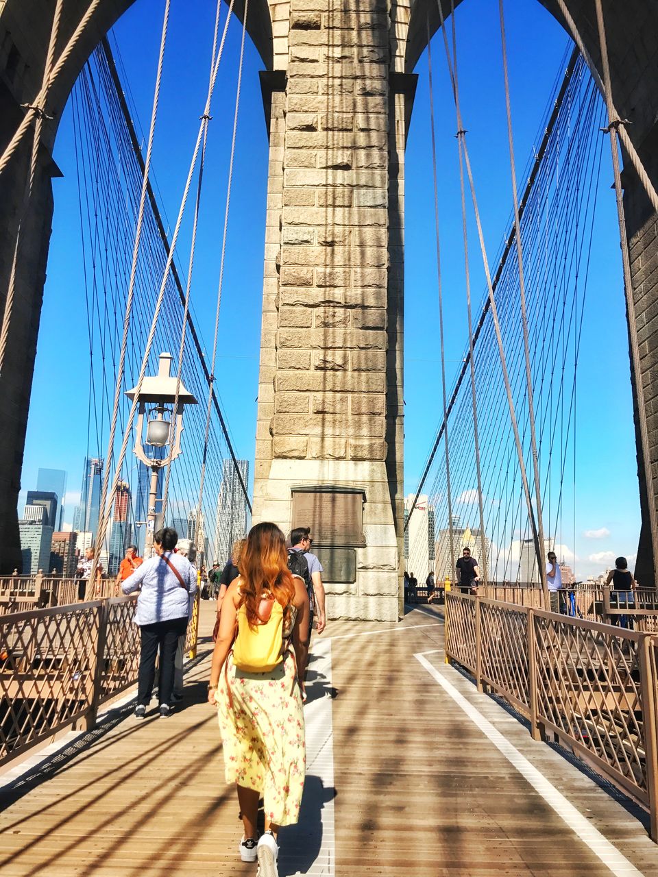 People on suspension bridge against sky in city