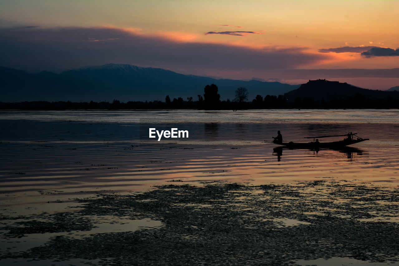 Silhouette man sitting in boat on lake against sky during sunset