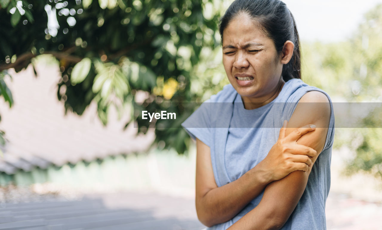 Woman touching shoulder in pain against trees