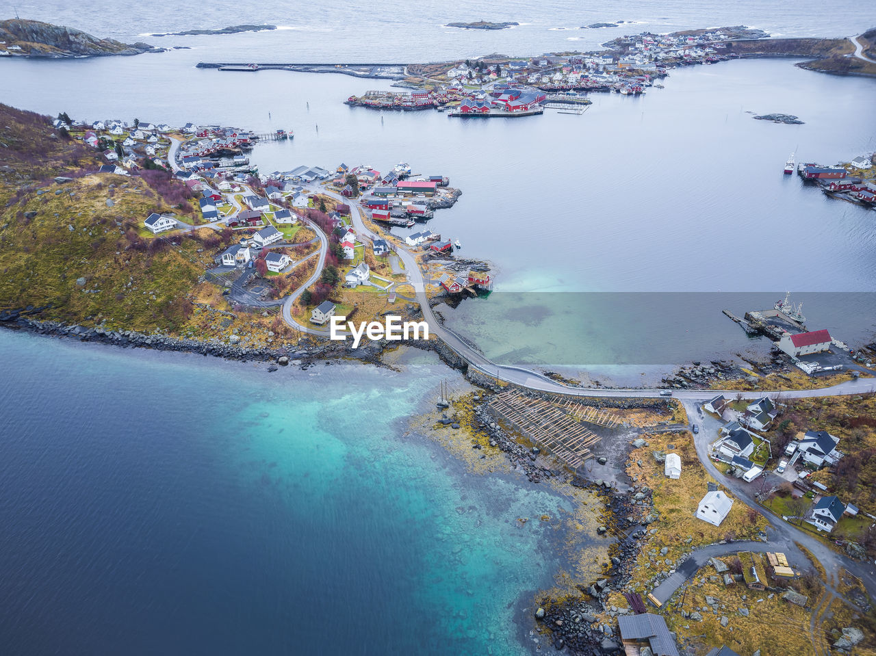 Drone view of residential buildings located on grassy lofoten islands with roads and bridge near calm clear sea in norway