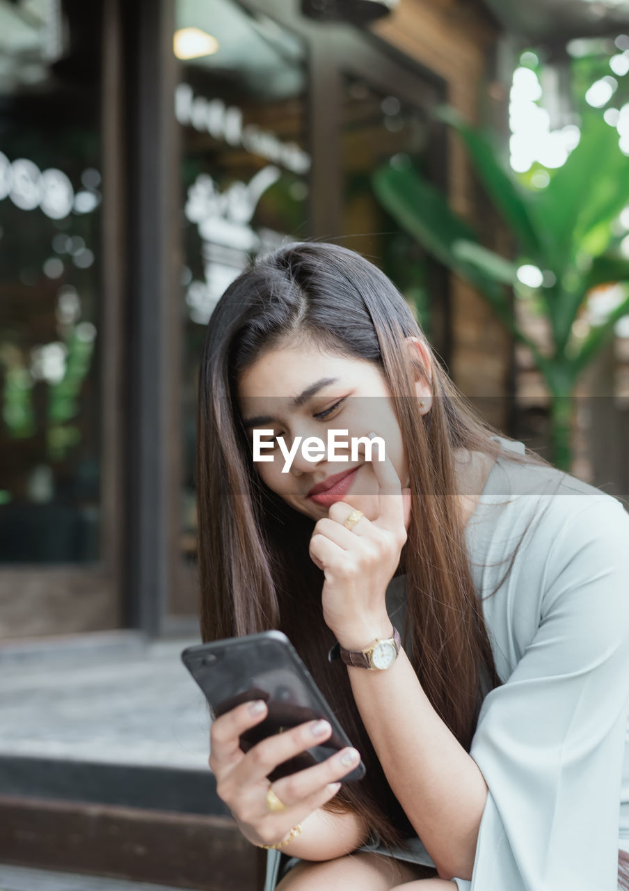 YOUNG WOMAN USING SMART PHONE WHILE STANDING ON CAMERA AT HOME