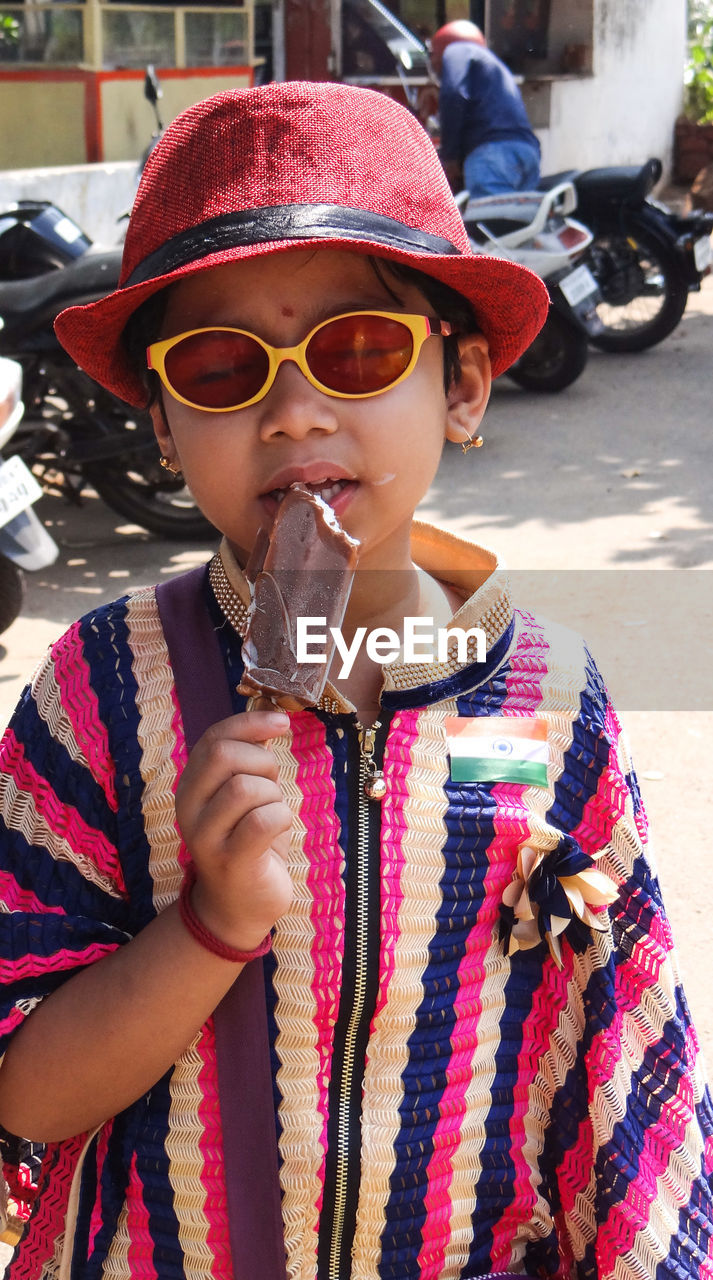 Girl eating popsicle while standing on footpath