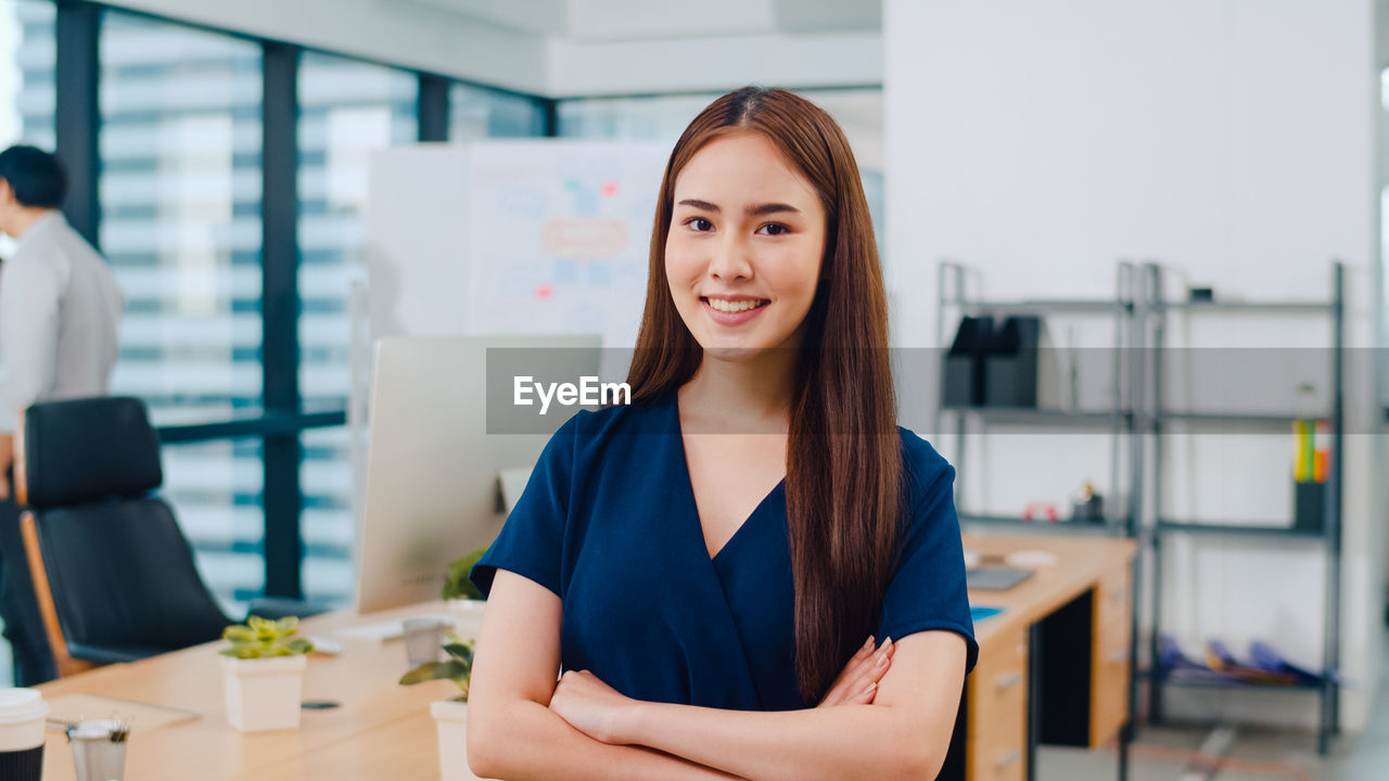 Portrait of smiling businesswoman with arms crossed standing in office