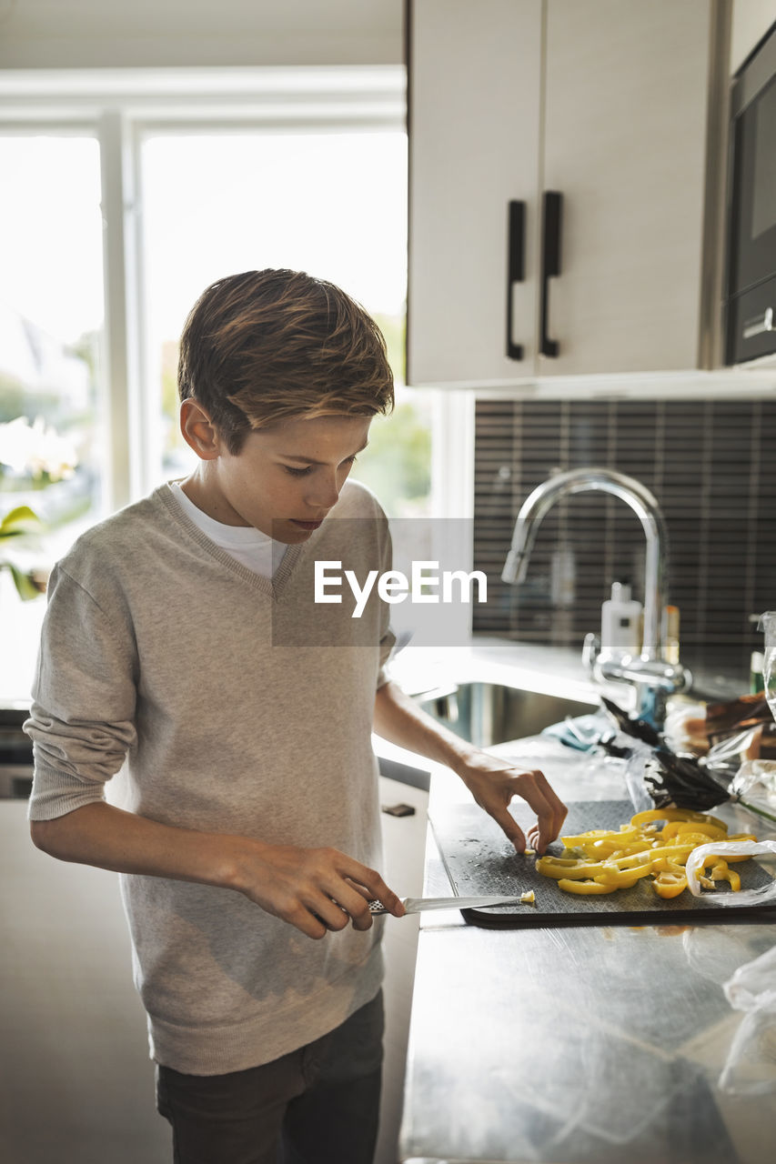 Boy cutting yellow bell pepper at kitchen counter