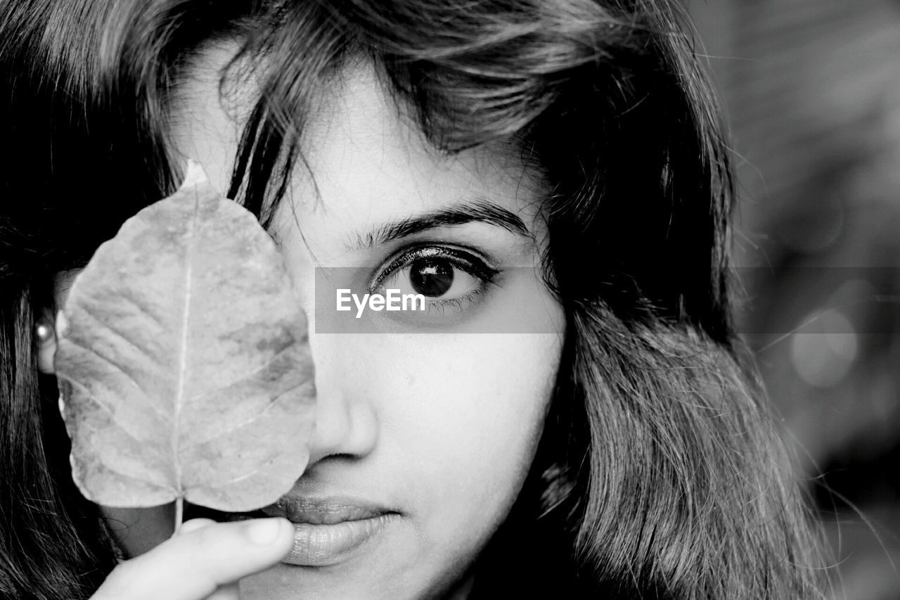 Close-up portrait of young woman holding leaf