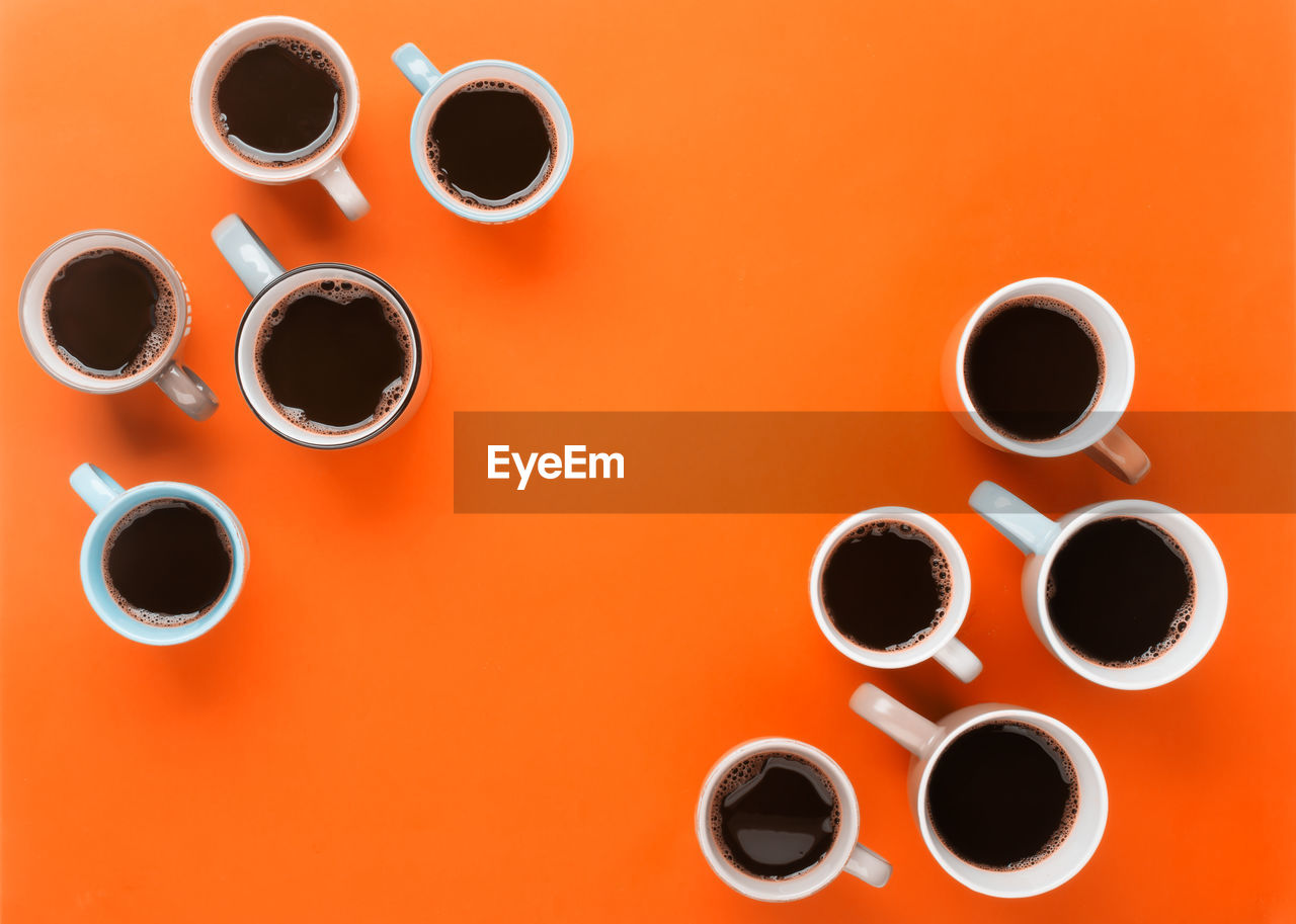 DIRECTLY ABOVE SHOT OF COFFEE CUPS ON TABLE AGAINST ORANGE BACKGROUND