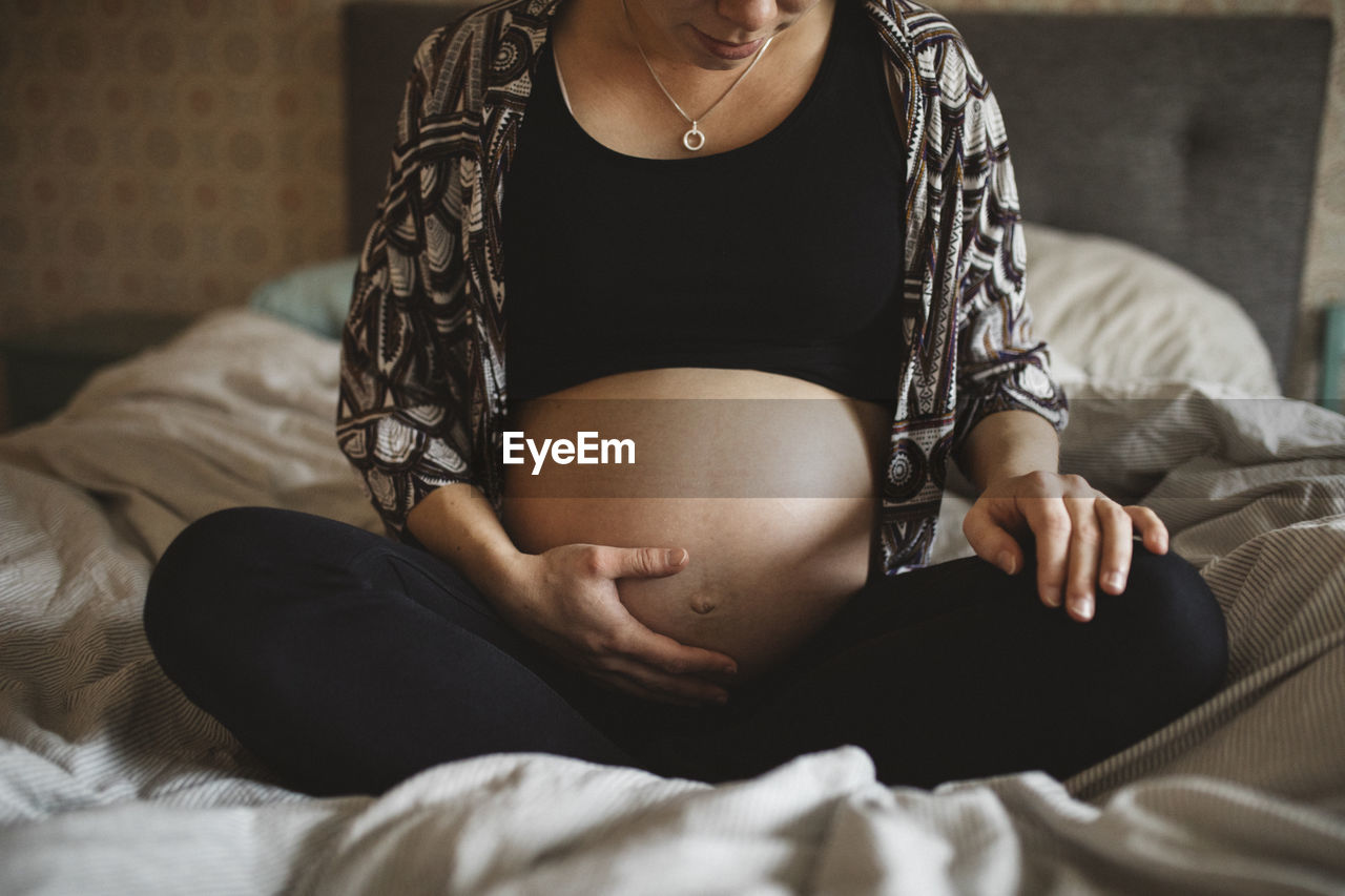 Pregnant woman sitting on bed and touching belly