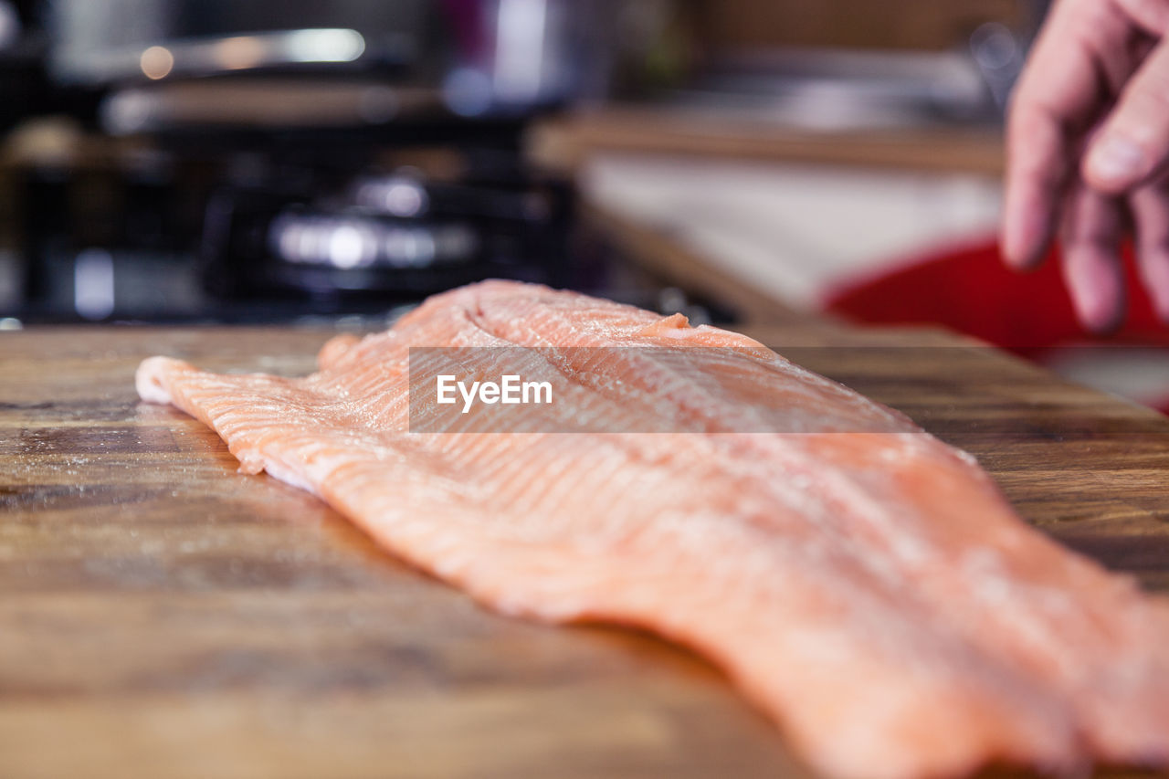 Cropped hand of man by fish on cutting board