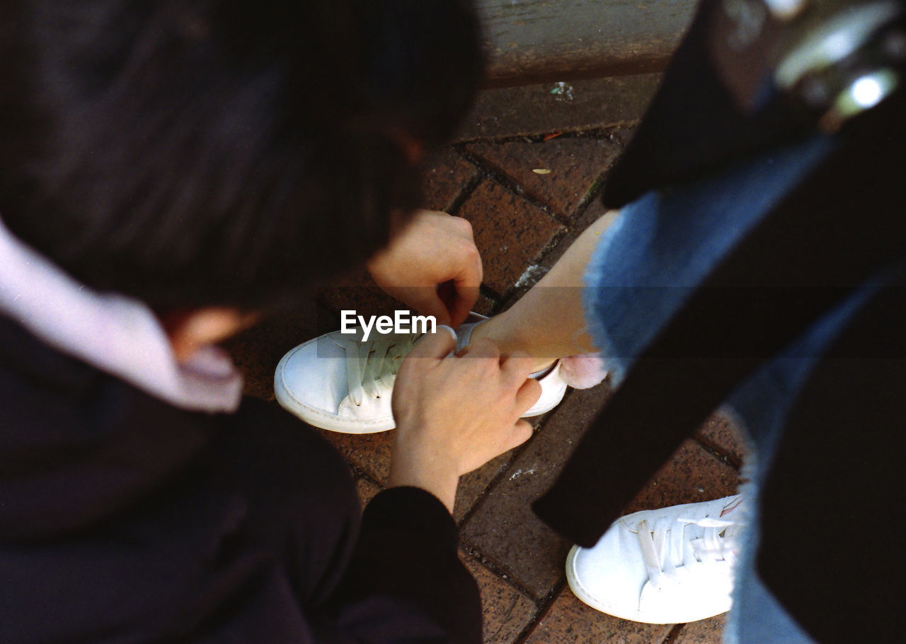 High angle view of man tying girlfriend shoe on footpath