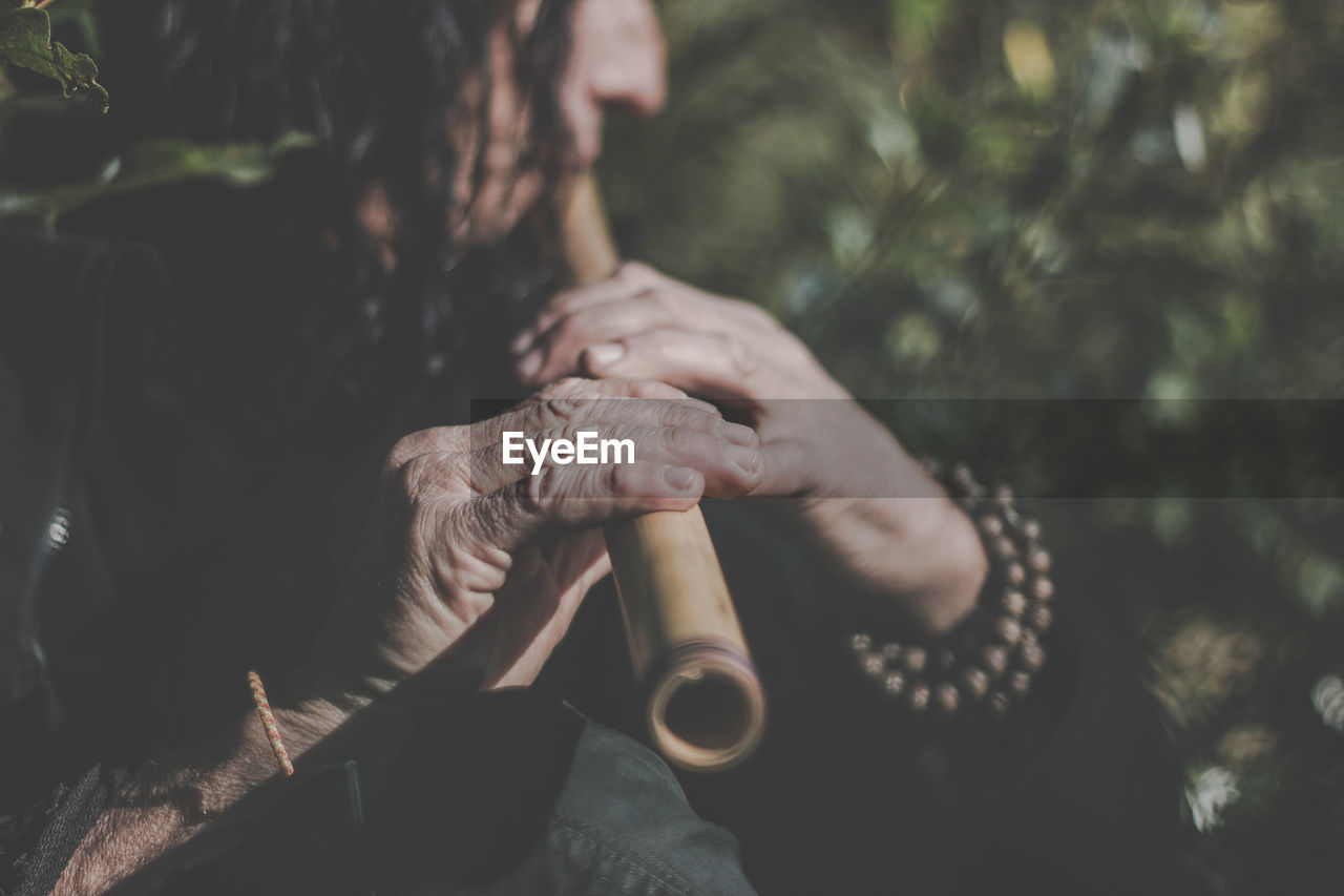 Midsection of man playing flute while standing in forest