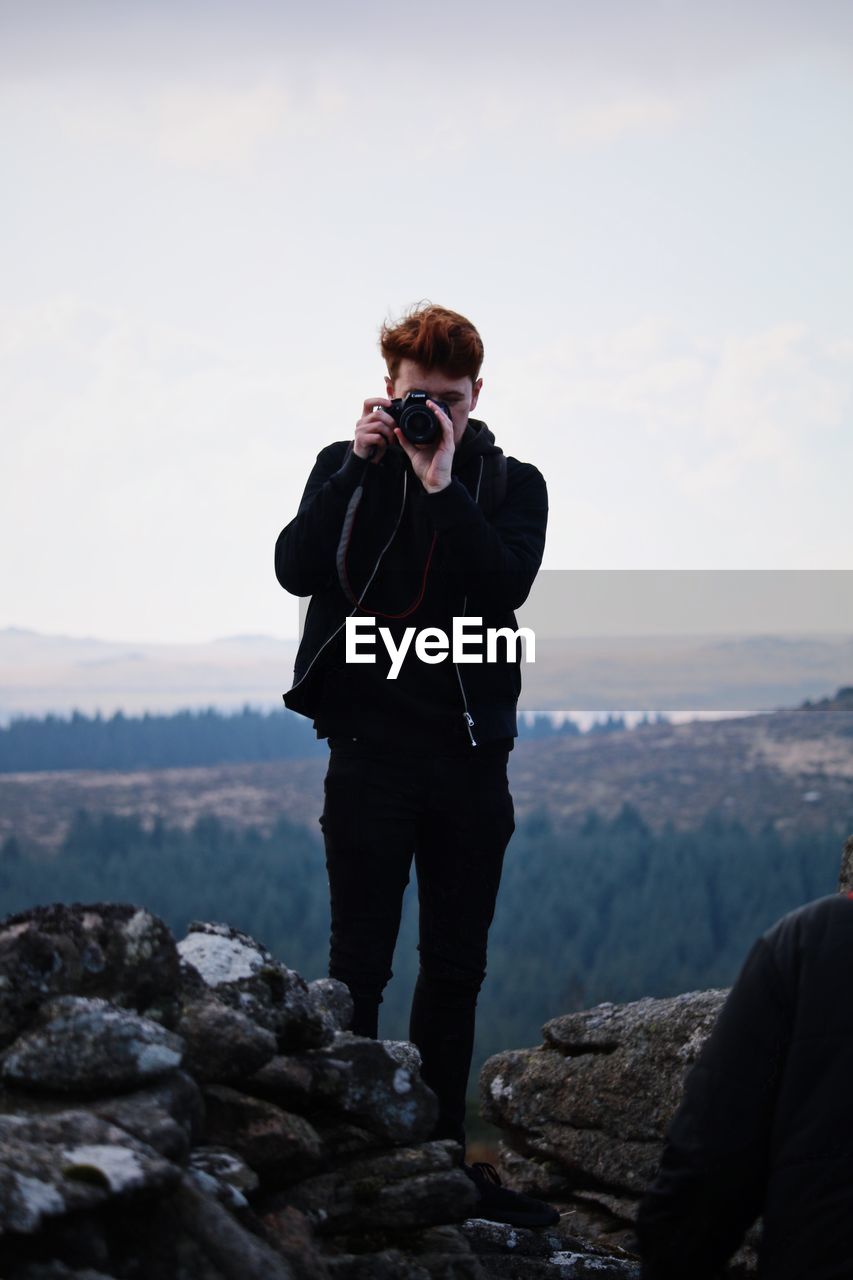 Man photographing on cliff against sky