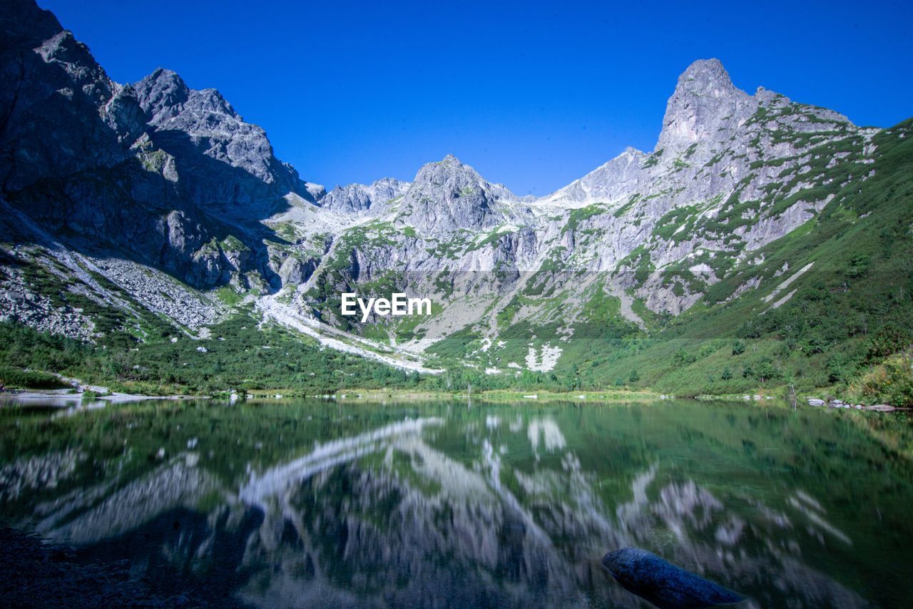 Scenic view of lake and mountains against clear blue sky