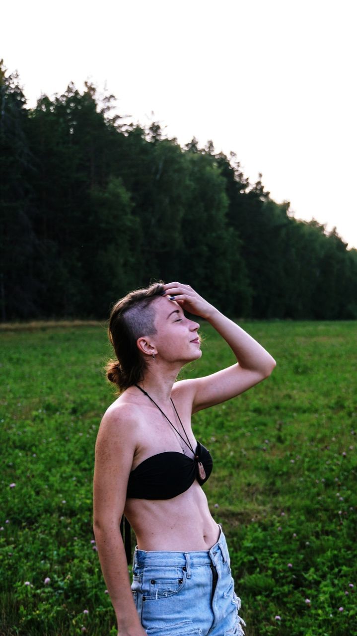 Sensuous woman standing on grassy field against sky