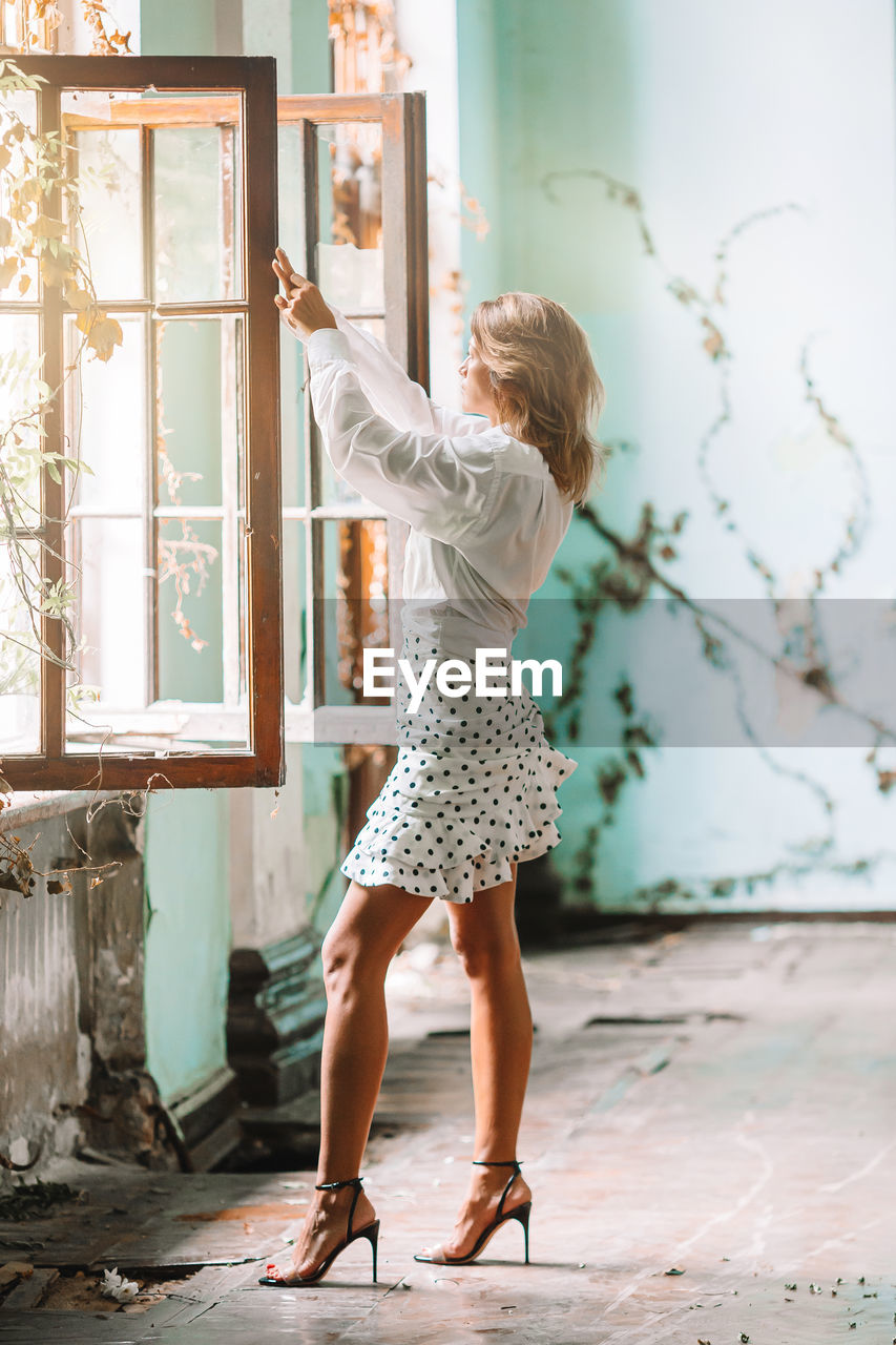 Side view of woman standing by window at abandoned home