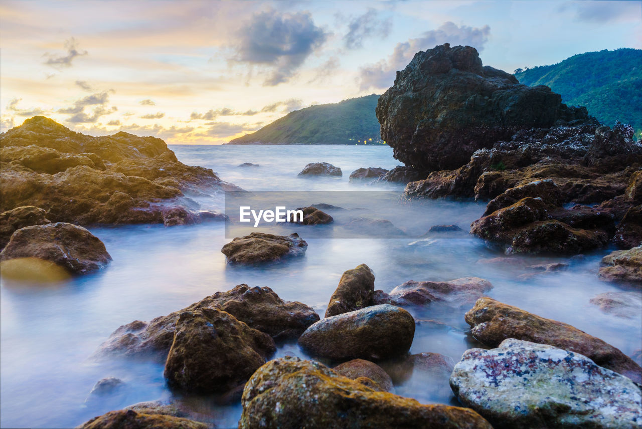 Rocks at sea shore against sky during sunset