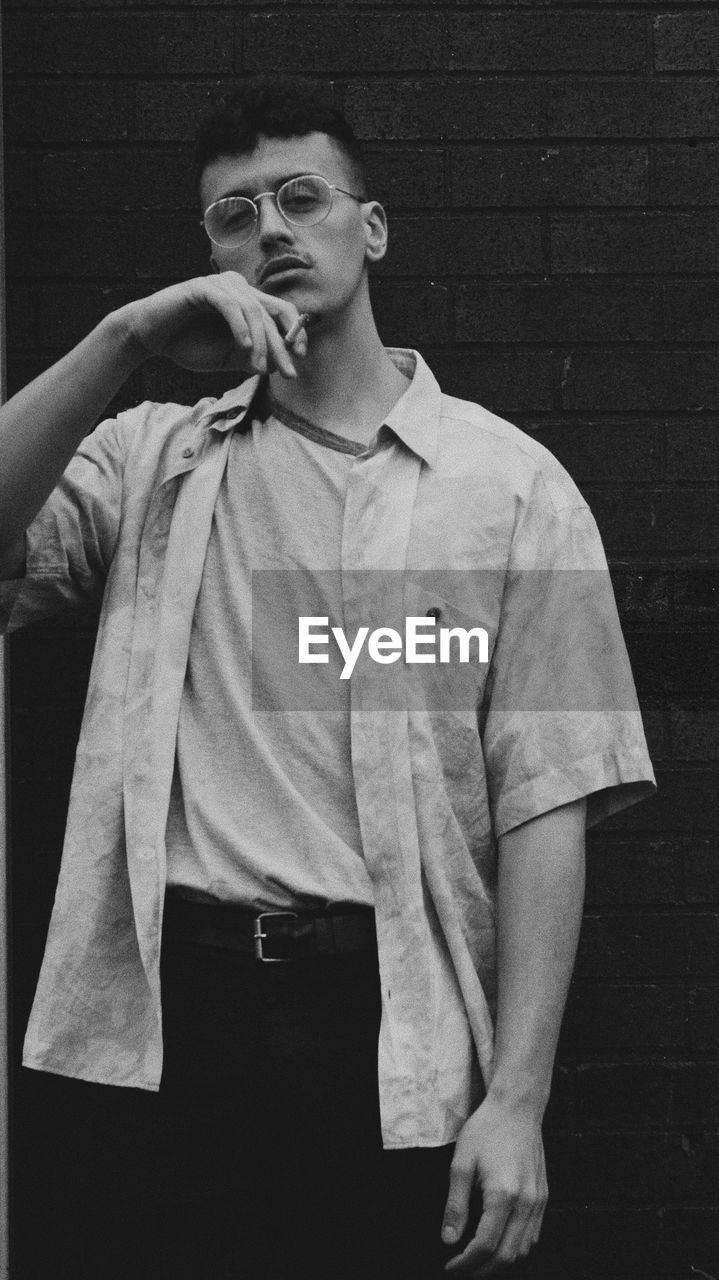 Portrait of young man with cigarette standing against wall