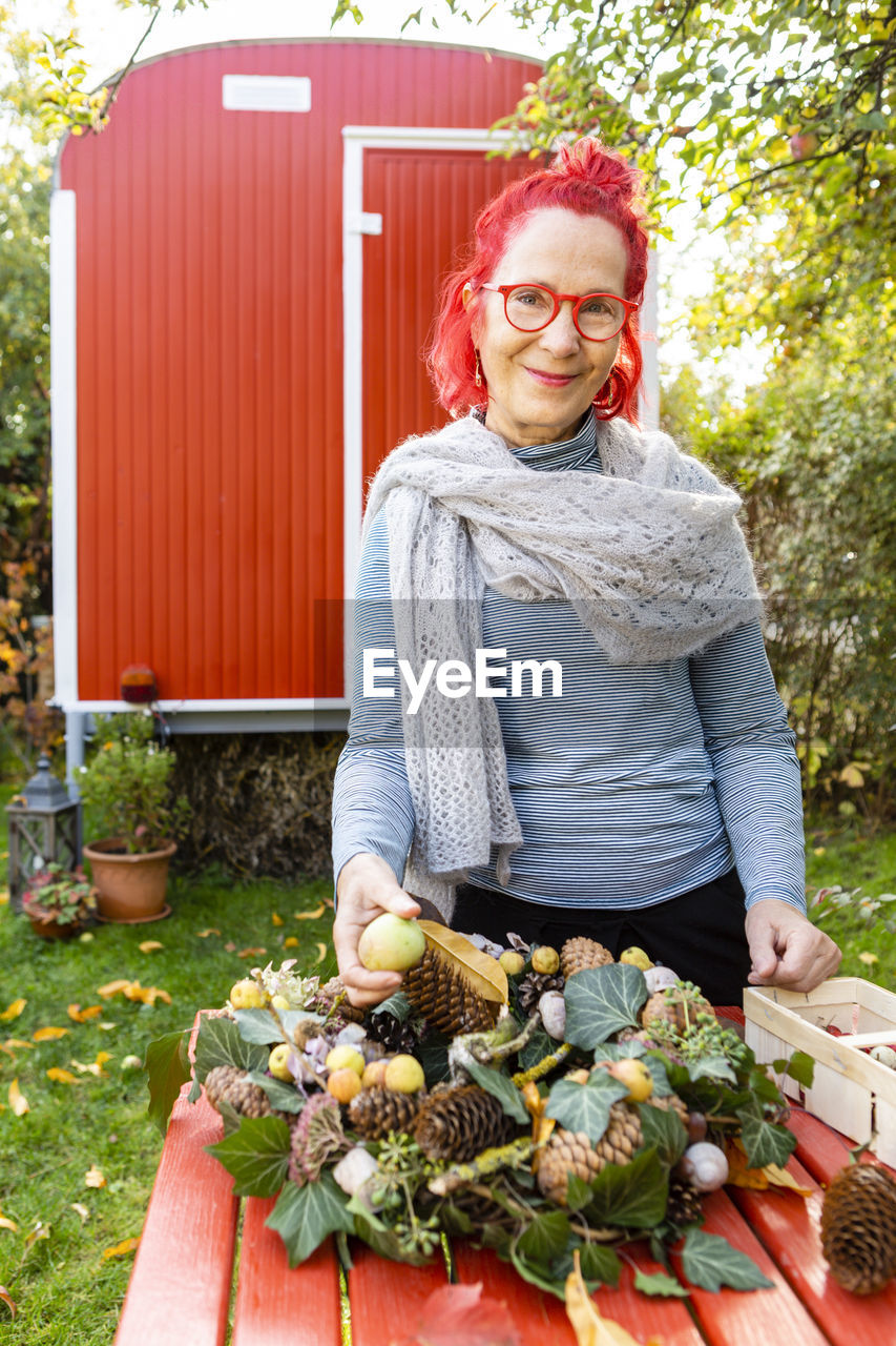 Portrait of smiling senior woman with red dyed hair tinkering autumnal decoration in the garden