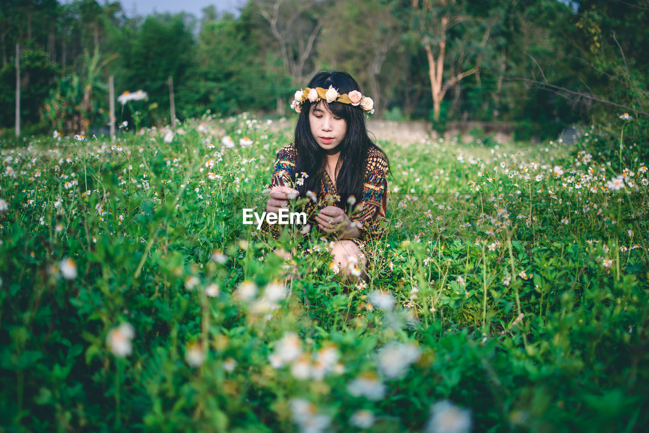 Woman wearing flowers while sitting on field 