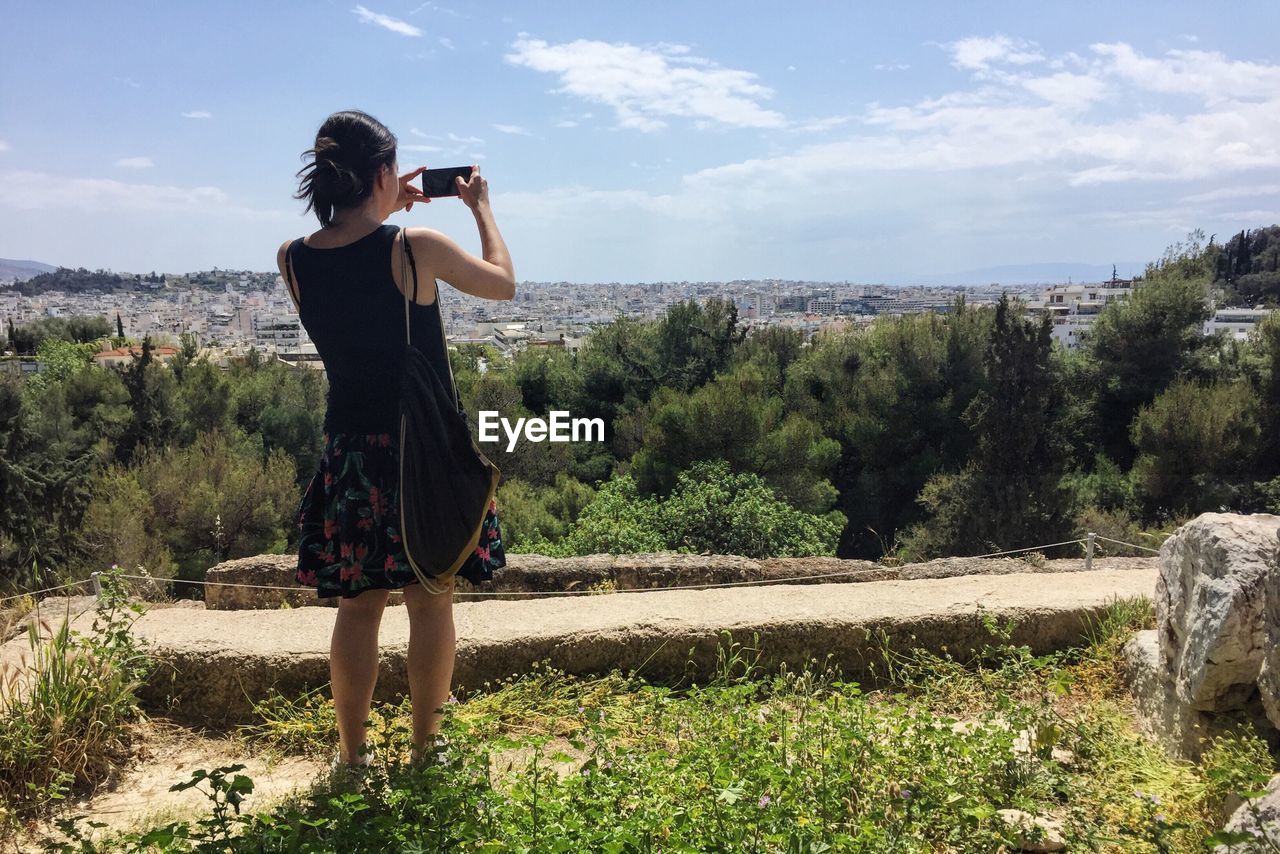 Rear view of woman photographing while standing on mountain against cloudy sky