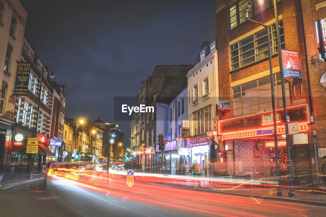 LIGHT TRAILS ON CITY STREET AGAINST BUILDINGS AT NIGHT