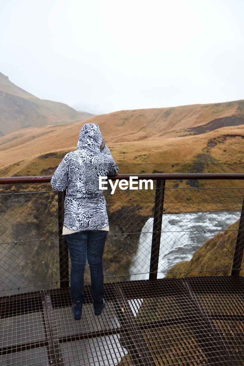 REAR VIEW OF WOMAN STANDING ON MOUNTAIN