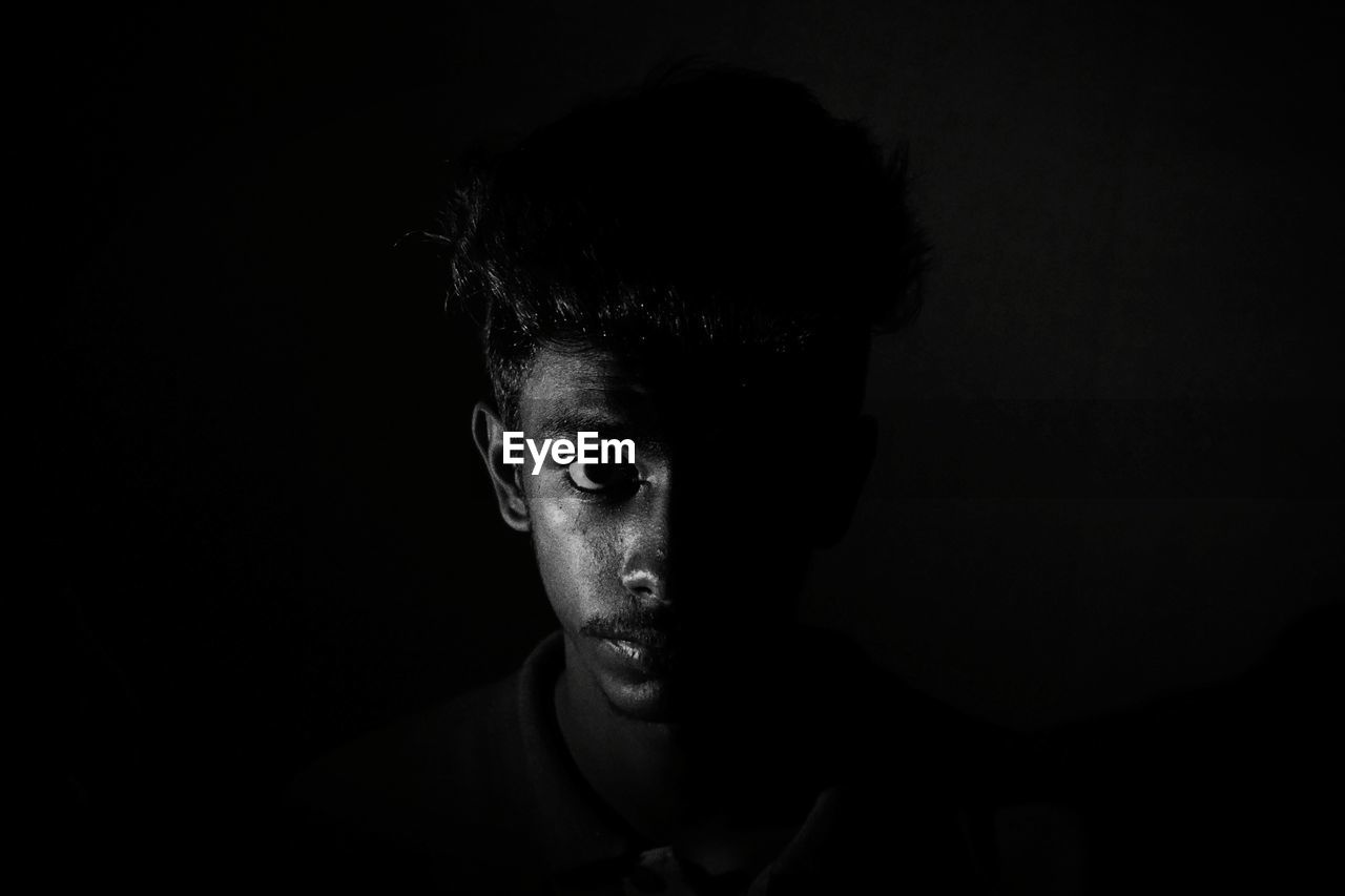 Young man looking away while standing against black background