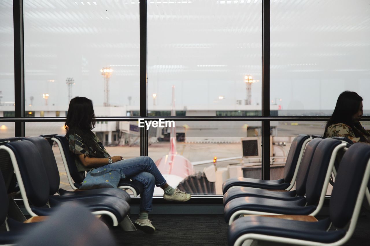 Women sitting on chairs at airport departure area