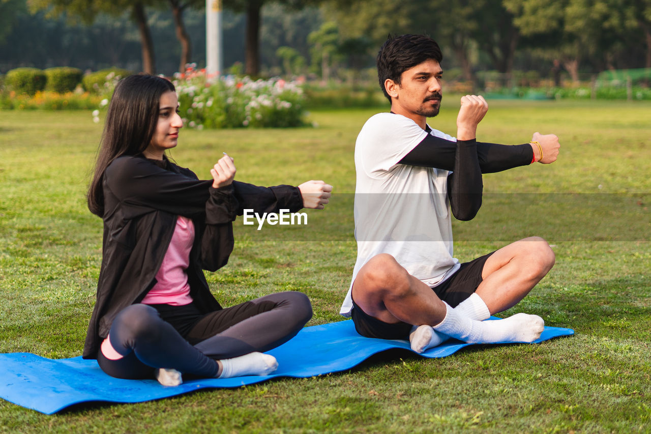 side view of young woman using mobile phone while sitting on field