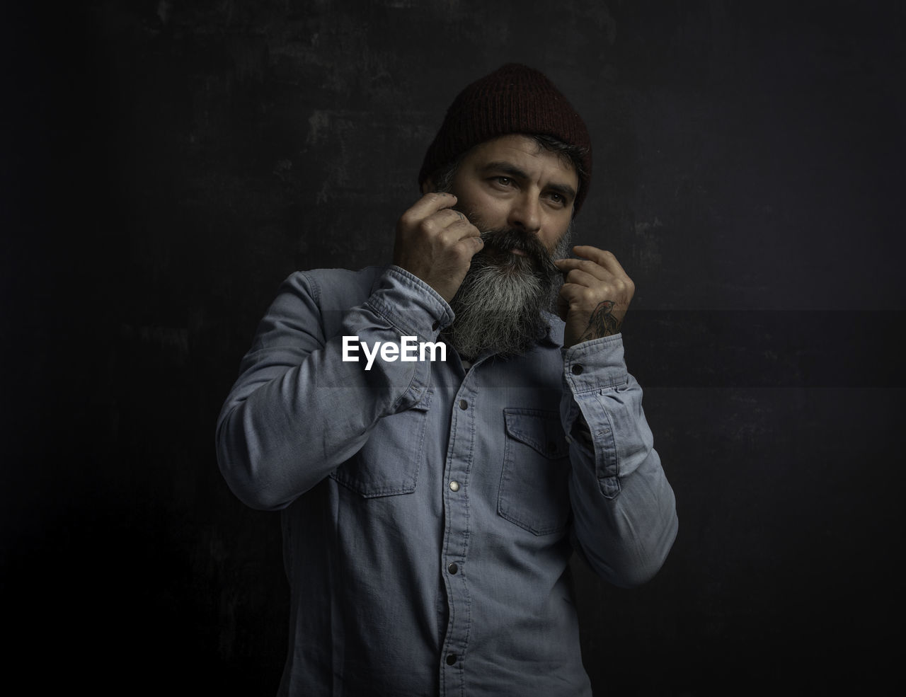 Portrait of handsome smiling man with beard sticking his mustache jeans shirt and wool hat.