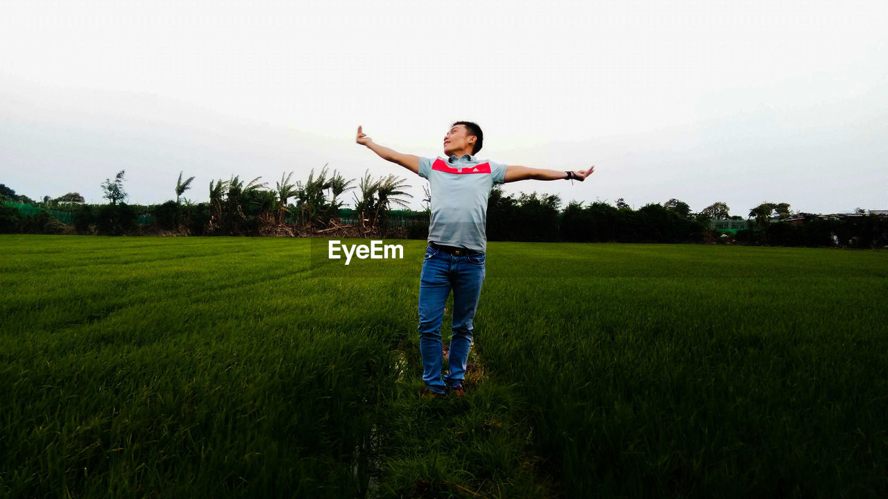 WOMAN STANDING ON FIELD AGAINST SKY