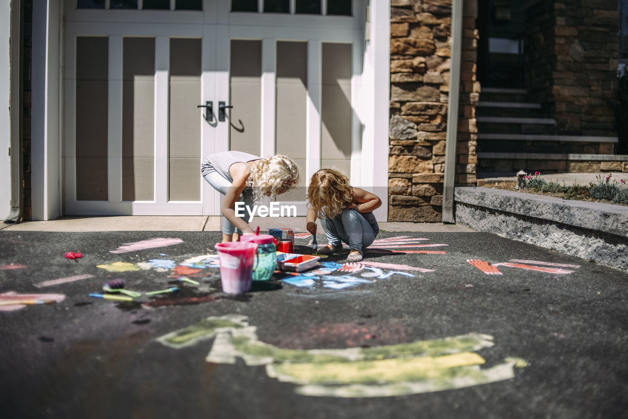 Playful sisters painting on asphalt in front of house during sunny day