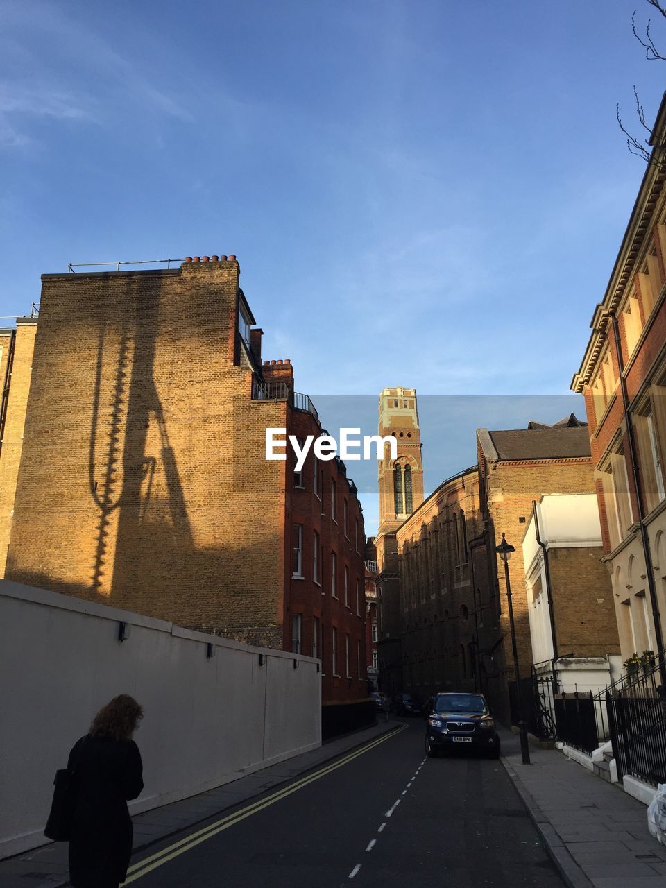 Rear view of woman walking on street by buildings against sky