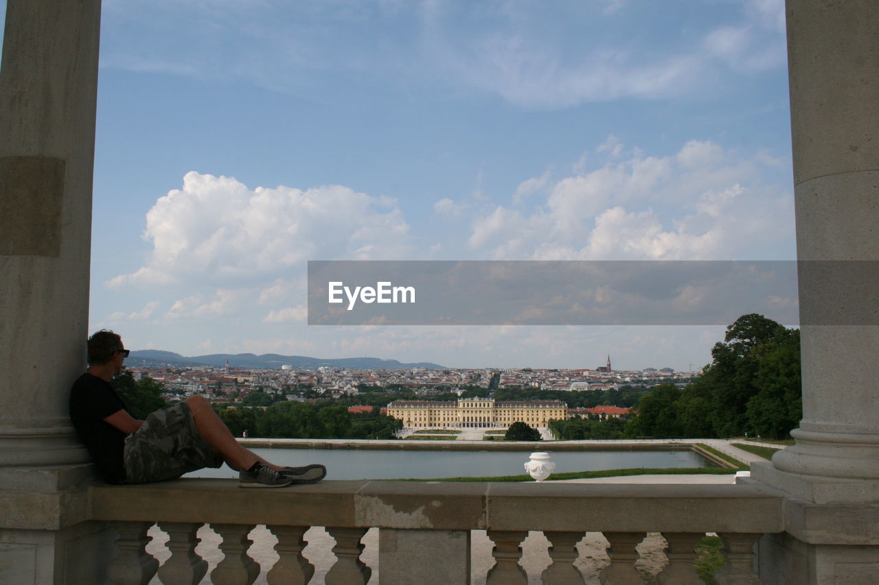 Man sitting on retaining wall against cityscape 