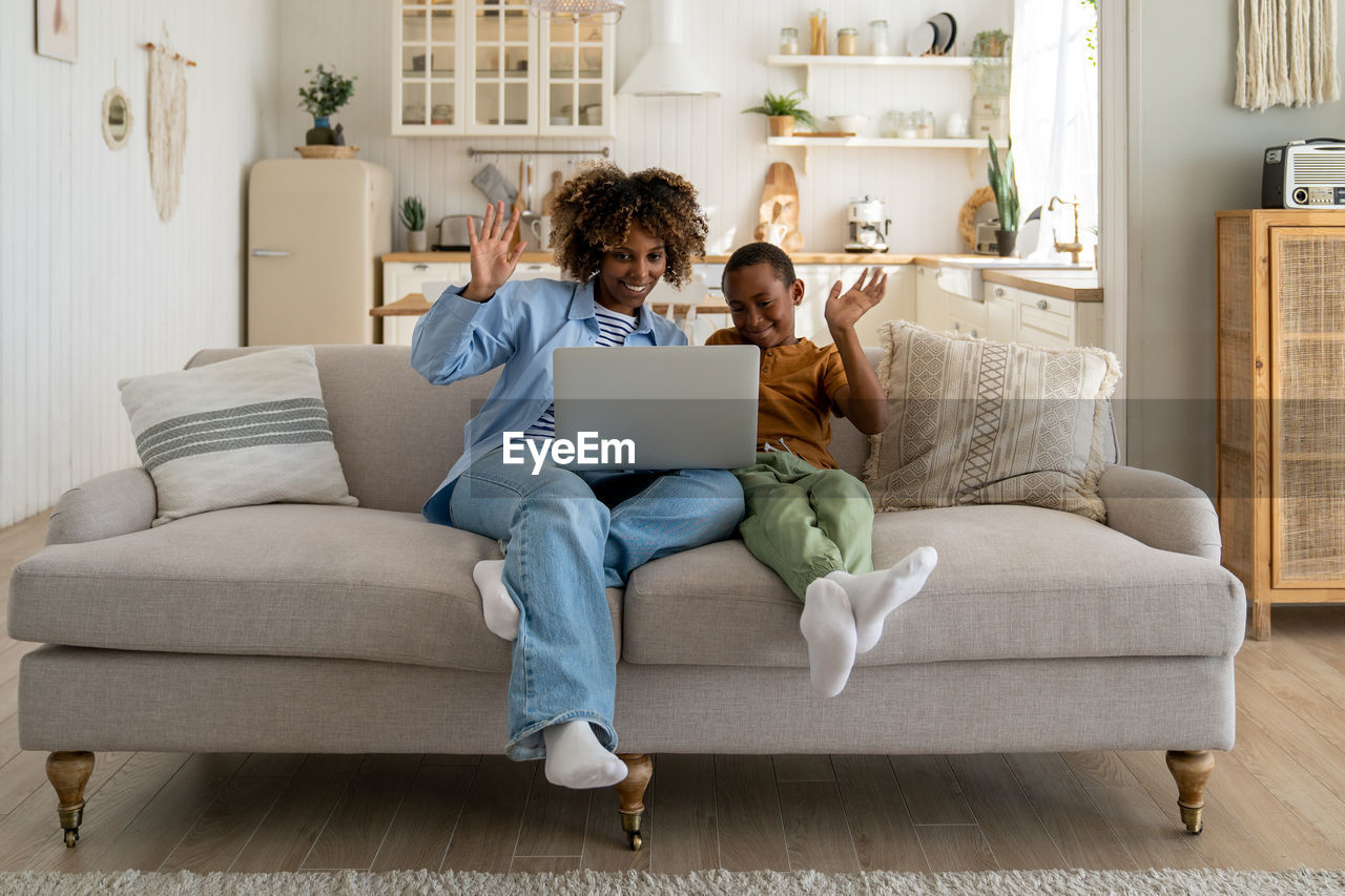 African american mother and kid son looks at web camera laptop for video call at home. happy family